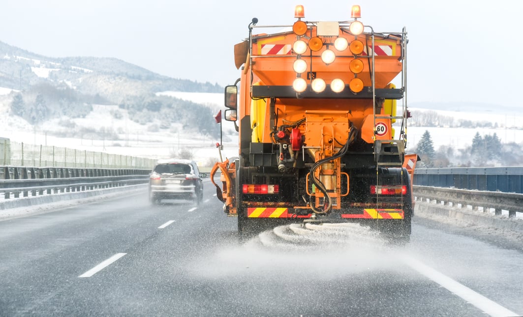 Snow plow on highway salting road.